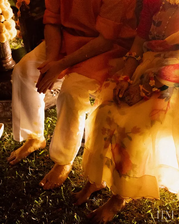 A candid detail shot from a Haldi ceremony. The couple's feet, covered in turmeric, and their intertwined hands tell a story of togetherness and tradition.