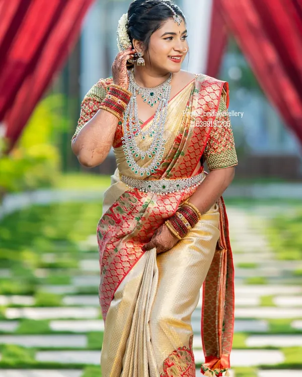 This is one of my favorite complete bridal looks. This bride is radiant in a full American Diamond (AD) stone set, including a layered haaram, choker, matching earrings, and a delicate vaddanam (waist belt) that perfectly complements her silk saree.
