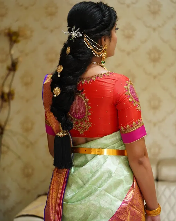 A detailed view of a traditional South Indian bridal braid. This hairstyle features intricate weaving and is adorned with classic gold accessories, creating a look of timeless elegance.