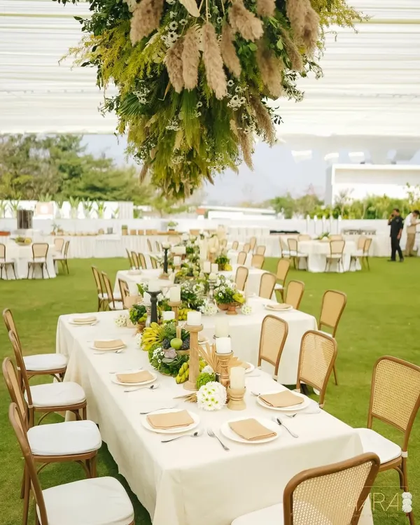An overview of our 'Easy Breezy Brunch', designed with sustainability in mind. The long tables are set on a lush green lawn, with hanging installations of pampas grass and natural greenery creating a canopy overhead.