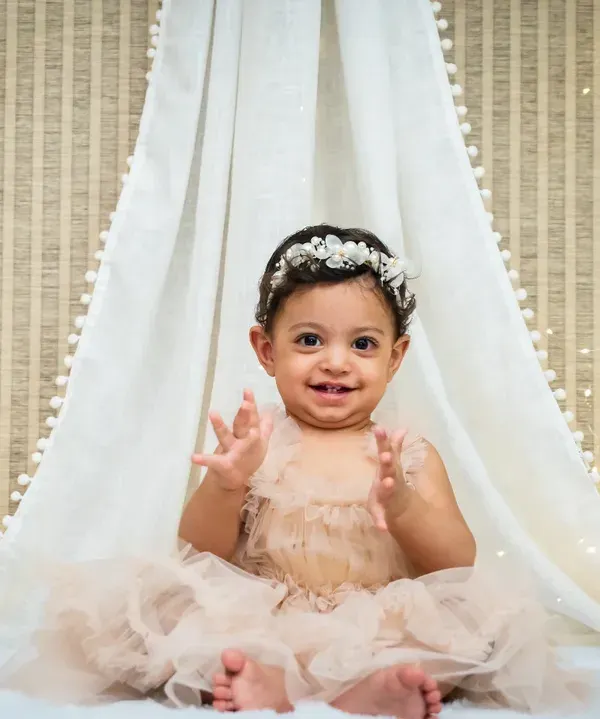 A beautiful close-up of a one-year-old girl in a peach tutu, clapping her hands with joy in a bohemian-style teepee setup.