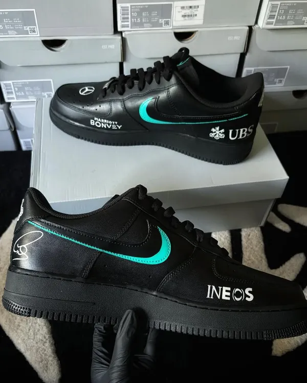Custom Nike Air Force 1s designed with a Lewis Hamilton Mercedes AMG F1 theme. This pair features sponsor logos like INEOS and UBS, showcasing our ability to execute precise corporate branding.