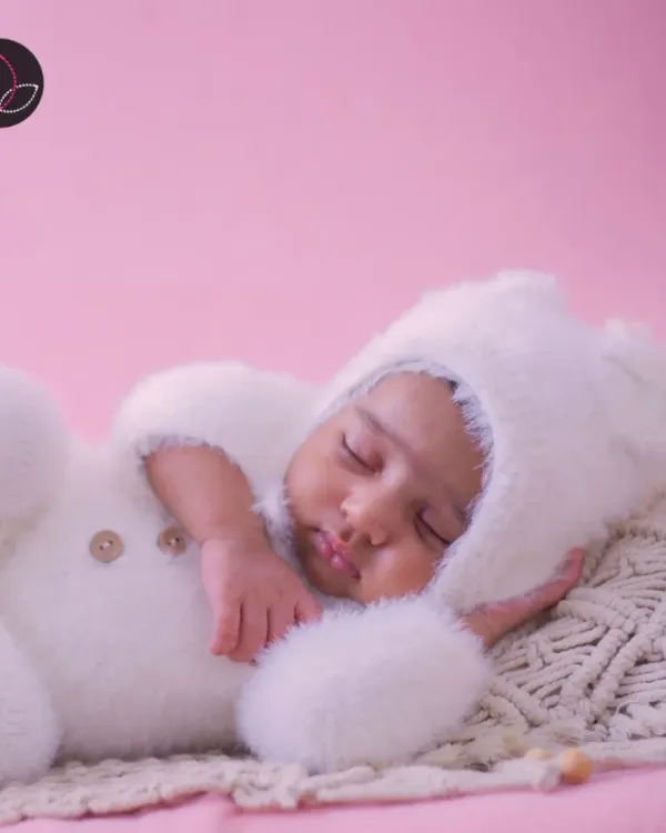 An adorable newborn portrait featuring a sleeping baby dressed in a fluffy white bunny outfit, looking perfectly cozy and peaceful.