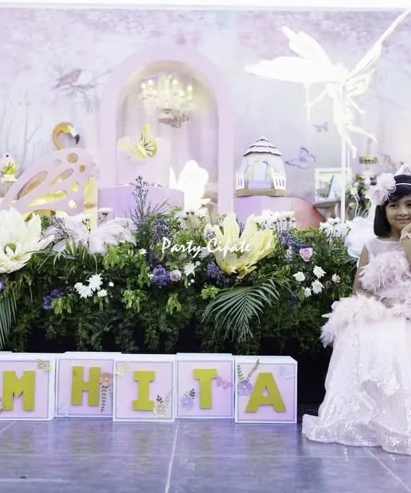 The birthday girl herself, looking like a real fairy princess in the enchanted garden I created. Seeing her smile in front of the personalized 'SAMHITA' name blocks and the detailed backdrop makes all the hard work worthwhile.