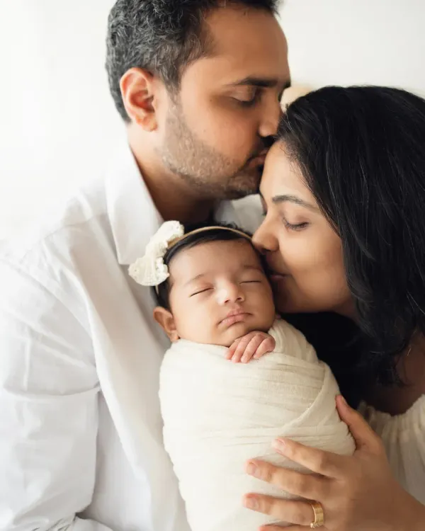 A father and mother gently hold their swaddled newborn, sharing a quiet moment of love. This is the kind of pure, simple connection I aim to capture in my newborn and parent photoshoots.