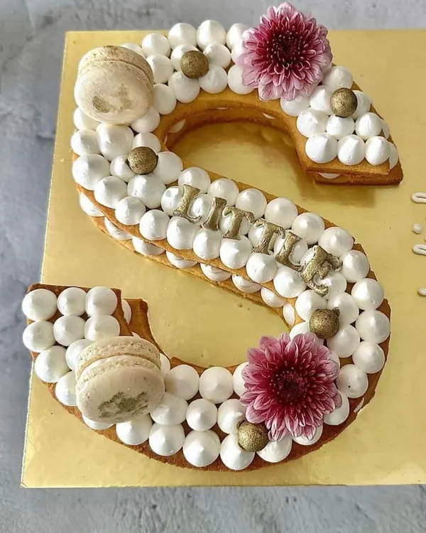 A personalized monogram tart cake for a Rakhi celebration. This 'S' shaped tart is made with a crunchy biscuit base and topped with cream, macarons, and fresh flowers.