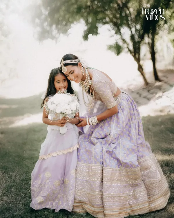 A bride in a beautiful lavender lehenga shares a sweet moment with a young flower girl. This image captures the magical connection between generations at a wedding.