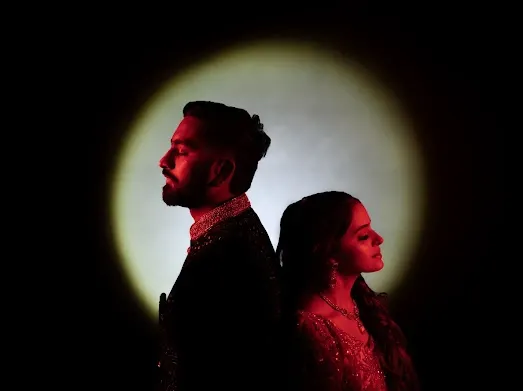 A creative couple portrait using a spotlight effect. The dramatic lighting and back-to-back pose create a modern and artistic image.