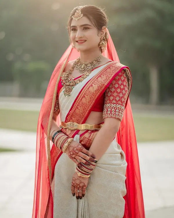 My beautiful bride Rachana, looking radiant in her red and white wedding saree. The custom blouse features a traditional check pattern with delicate embroidery on the sleeves.