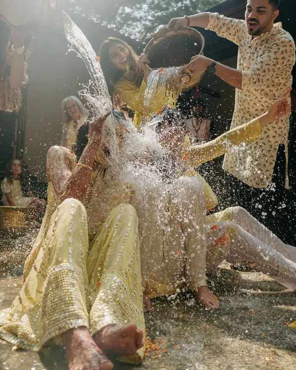 The moment the Haldi ceremony turns into a water fight. This shot of pure, uninhibited fun captures the joyous chaos and laughter that make for the best memories.