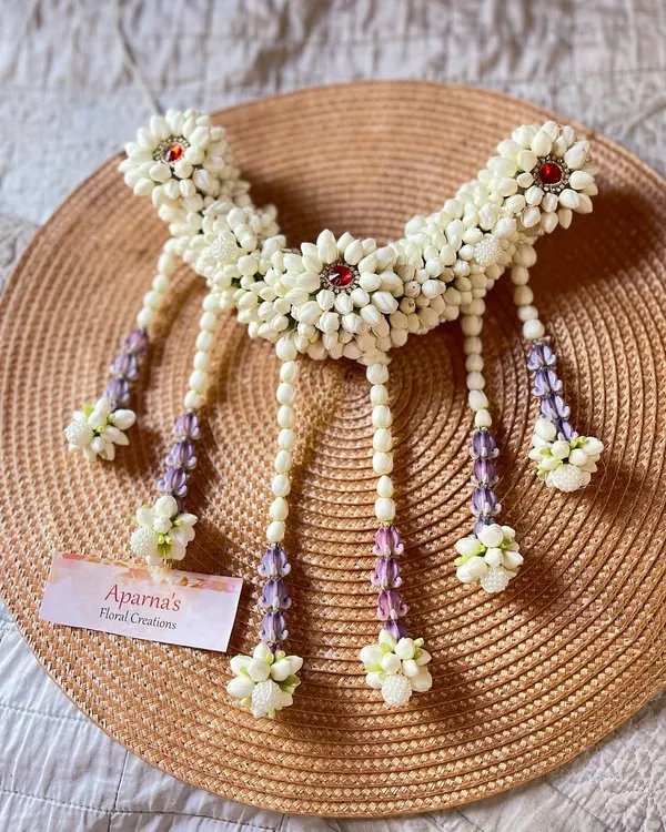 A beautiful floral hair brooch made from white jasmine buds. This piece can be worn with a bun or braid and is accented with red stones and delicate hanging strands.
