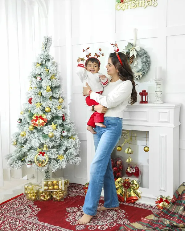 A full-length view of our Christmas-themed studio setup, showing a mother lifting her child in joyful celebration. The festive decor, from the frosted tree to the fireplace, creates a complete holiday scene for memorable family photos.