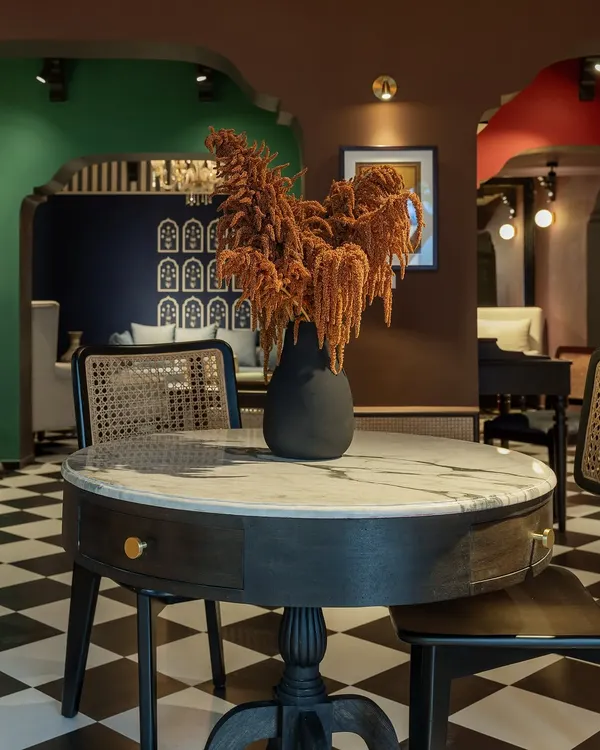 This setting from our House of Goya experience center features a marble-topped pedestal table and a caned chair against a backdrop of rich, layered colors. It demonstrates how we mix classic forms with bold, modern palettes.