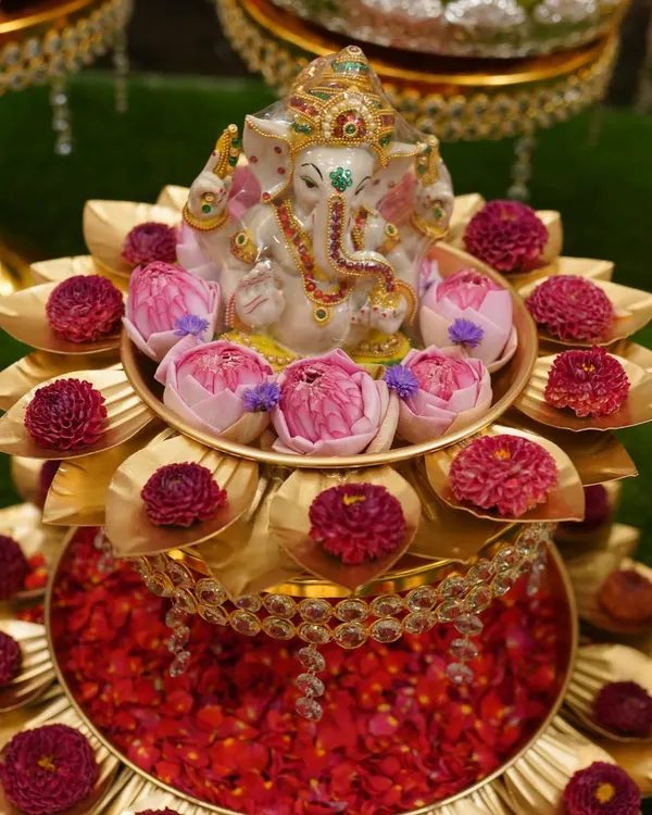 A beautiful two-tiered brass stand with a Ganesha idol, surrounded by fresh lotus buds and gomphrena flowers. This is a perfect pooja centerpiece.