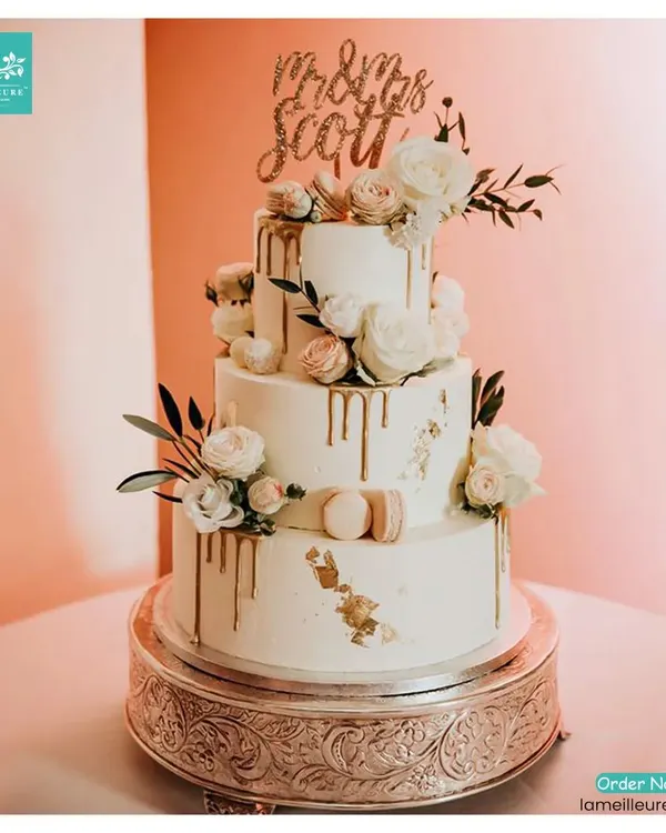 A stunning three-tiered custom wedding cake. This elegant creation features a white buttercream finish, a delicate gold drip, and is adorned with fresh flowers and macarons.