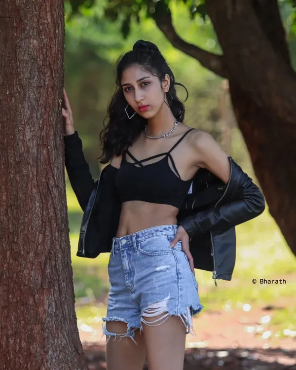 A classic street style look featuring a black crop top, leather jacket, and distressed denim shorts. The outdoor park setting with natural light gives it a relaxed, cool vibe.