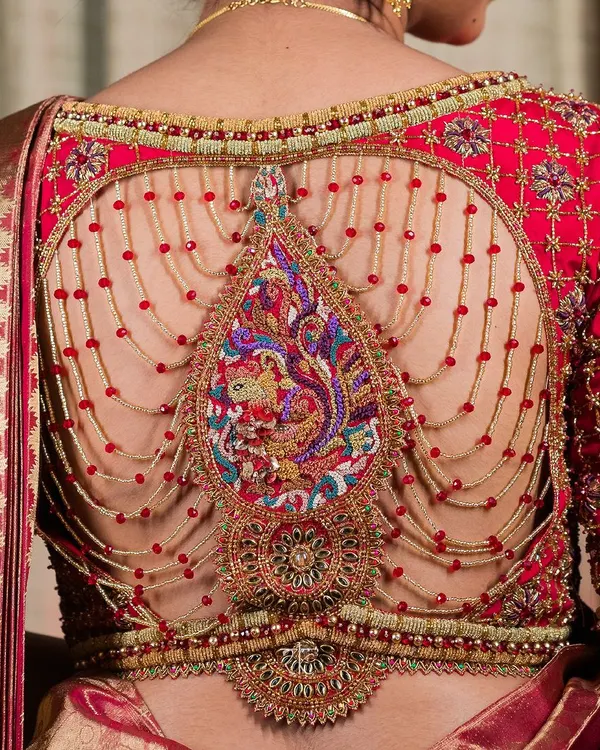A masterpiece of artistry, this bridal blouse back features a breathtaking peacock motif, intricately rendered in multi-colored threadwork and zardosi. The design is framed by delicate, cascading chains of red beads, creating a piece that is as much a jewel as it is a garment.