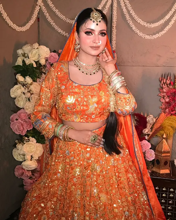 "Subhanallah." A beautiful portrait in a vibrant orange lehenga. The makeup is soft and glowing, with a focus on defined eyes and a traditional maang tikka.