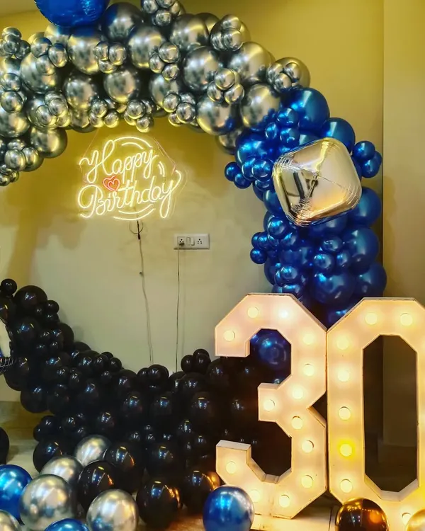 Hum har tarah ki milestone birthday party ke liye decoration karte hain. Yeh 30th birthday ka setup hai jisme humne chrome blue, black, aur silver balloons ka ring banaya hai. Saath mein '30' number wala light letter aur 'Happy Birthday' ka neon sign bhi hai.
