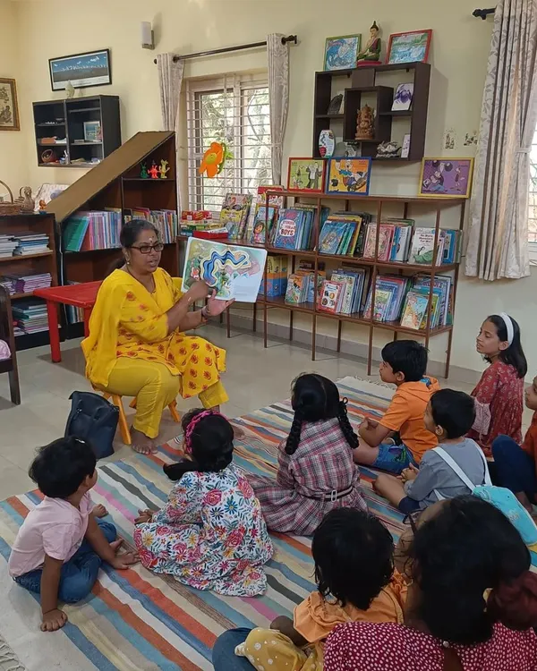 A storyteller captivates a group of young listeners with a beautifully illustrated book. We ensure every child feels included, sitting together on our colorful floor mat for a shared experience.