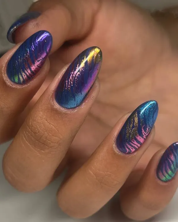 A stunning multi-chrome nail art design. The metallic polish shifts between shades of blue, purple, and gold, with a subtle zebra-like pattern etched on top for added texture.