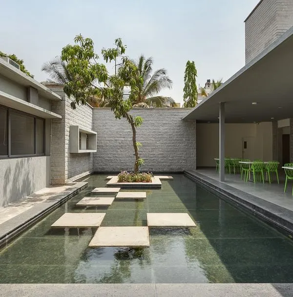 The canteen at the KIPCER building in Bengaluru, opening onto a tranquil water court. The design provides a calm, restorative space for staff and visitors, with stepping stones and a single tree creating a focal point.