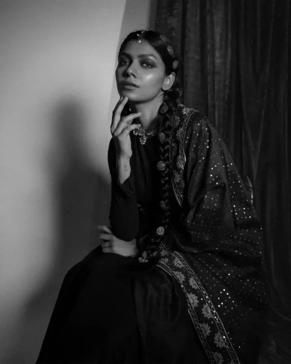 A moody, black and white portrait from the 'Amodini' series. This look features a dark Anarkali with an embellished dupatta and traditional hair jewelry, creating a vintage, cinematic feel.