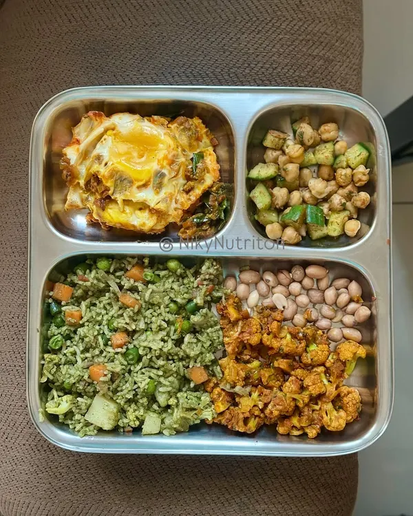 A true high-protein powerhouse plate. This meal features vegetable rice, a masala fried egg, roasted cauliflower, boiled peanuts, and a chickpea salad.