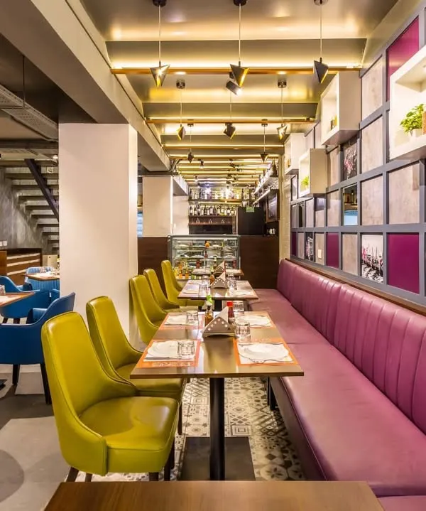 A long shot of the main dining hall at Pasta Street, Cunningham Road, showing the linear arrangement of seating. The combination of plush pink booth seating and colorful chairs creates a dynamic and comfortable environment for diners.