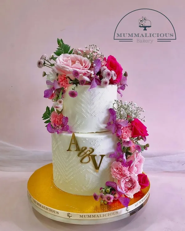 A cascade of fresh, vibrant flowers makes this two-tiered wedding cake a breathtaking centerpiece. The textured frosting and custom initial topper add a personal and modern touch to this romantic design.