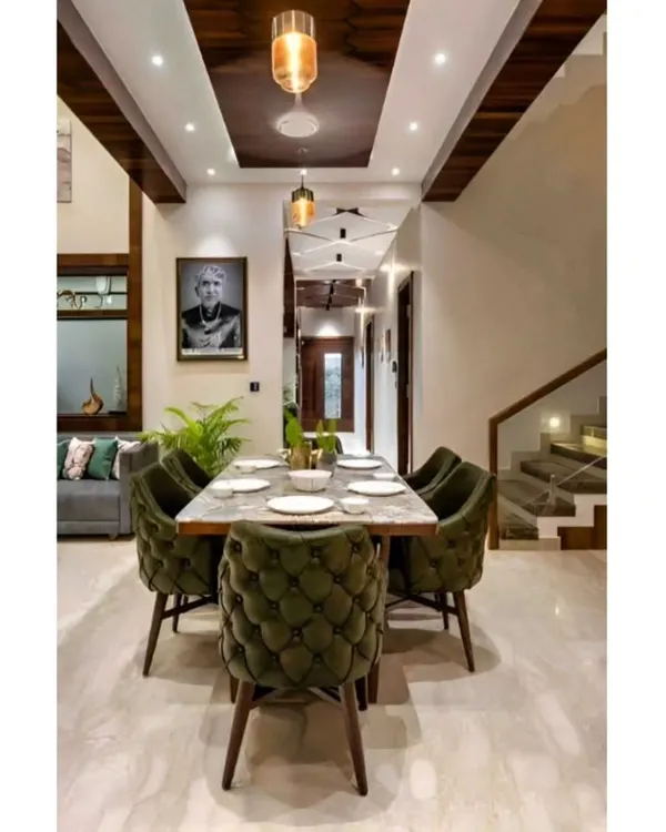 An elegant dining area designed for family gatherings. The space features comfortable upholstered chairs, a marble-top table, and a high ceiling with modern pendant lighting, creating a sense of grandeur.