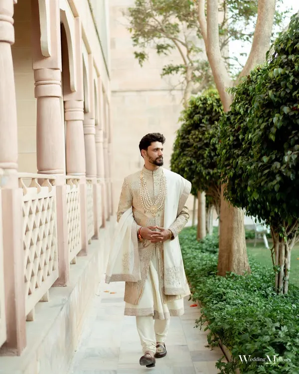 A classic portrait of the groom looking dapper in his wedding sherwani. Captured in a beautiful architectural setting, this photo exudes elegance and style.