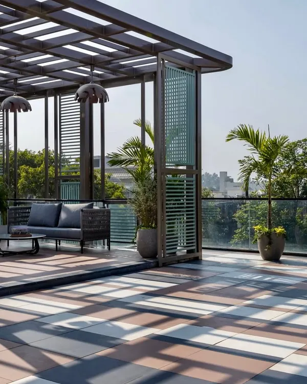 A perfect balance of shade and sun. This terrace in Faridabad features a slatted wooden pergola over a comfortable seating area, with large potted palms adding a touch of the tropics. The patterned floor tiles add a layer of visual interest to the design.