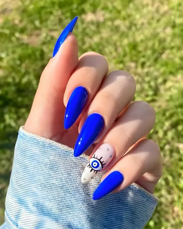 A bold and trendy look featuring vibrant cobalt blue gel polish on long stiletto extensions, with a detailed evil eye accent nail for a touch of personal style.