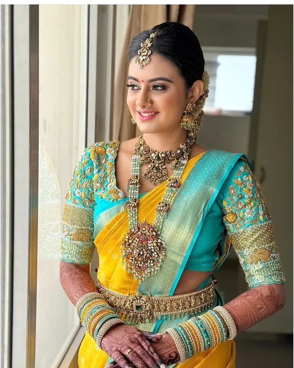 A full view of a bride looking radiant in our 92.5 silver-based bridal set with gold plating. The vibrant turquoise and yellow saree makes the intricate jewellery stand out beautifully.