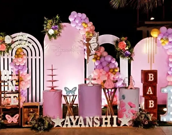 This is a complete first birthday setup I designed with a butterfly theme. It includes custom-arched backdrops, themed pedestals for the cake, balloon garlands in pastel shades, large "BABY 1" marquee letters, and wooden fencing to create a beautiful, enclosed photo zone.