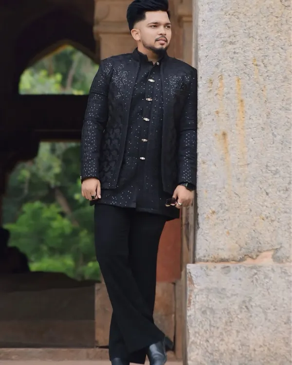 A model wearing a handcrafted black Indo-Western outfit. The layered look, with its textured jacket and tonal kurta, speaks power and elegance in every detail.
