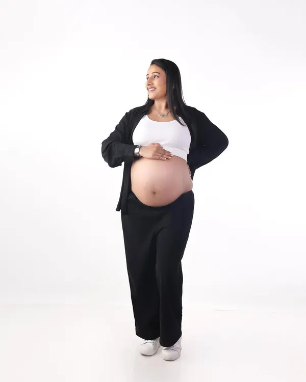 A simple and happy portrait against a clean white background. Dressed in casual clothes, this mom-to-be shows off her beautiful baby bump with a confident smile.