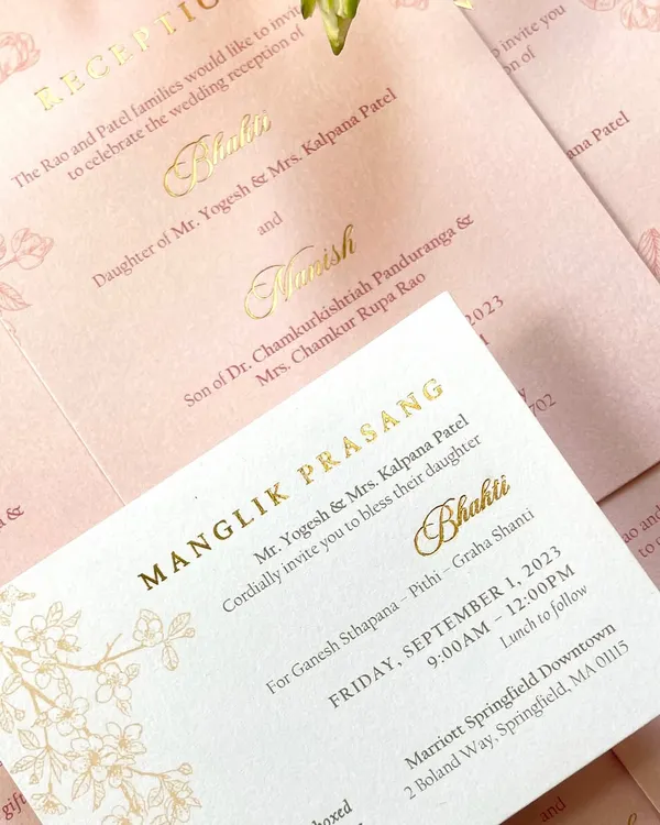 A close-up of a classic invitation with elegant gold foil lettering on soft pink and white cards. The delicate, line-drawn floral details add a touch of romance to the clean and timeless design.