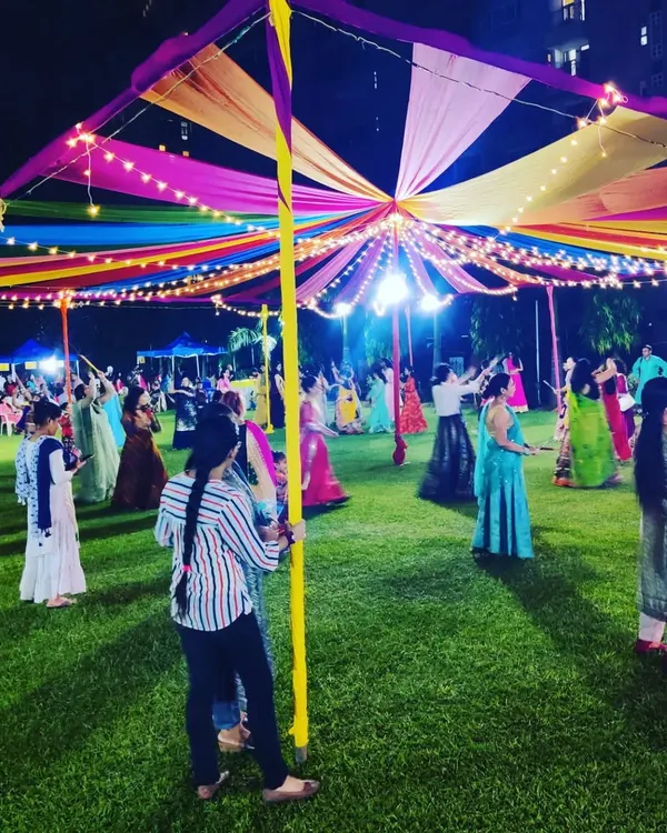 A wide shot of a Dandiya Night in full swing under the colorful canopy. This shows how the lighting and decor create a festive environment for guests to dance and celebrate Navratri.