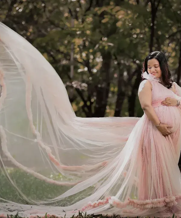 A breathtaking outdoor shot where the mom-to-be's pink gown and veil seem to float in the air. The natural park setting adds a touch of fairytale magic to this maternity portrait.