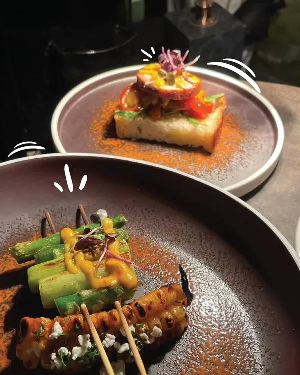 A display of our diverse international canapés. This pairing features grilled asparagus skewers with a creamy sauce and feta, alongside an open-faced toast topped with cured meat, showcasing our creative approach to global appetizers.