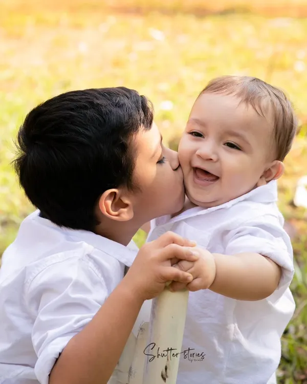 A beautiful family portrait outdoors, with a big brother giving his baby brother a sweet kiss on the cheek. These are the moments that matter.