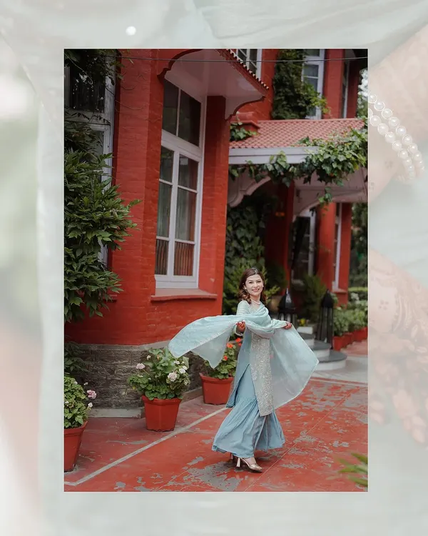 A candid shot of a woman in a beautiful blue sharara, twirling happily in the courtyard of a heritage hotel during her engagement celebration.