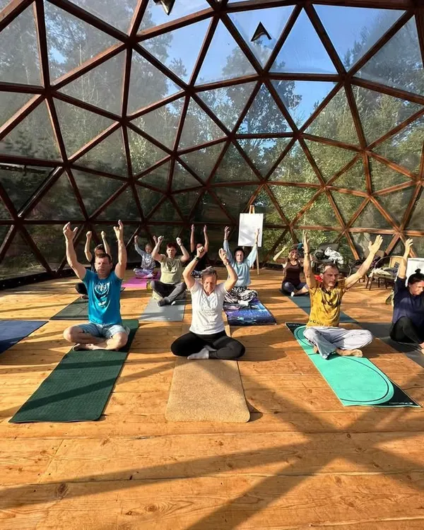 A group of students practicing a seated pose with arms raised, energizing the spine and opening the chest. This moment captures the collective energy and focus during one of our indoor yoga workshops.