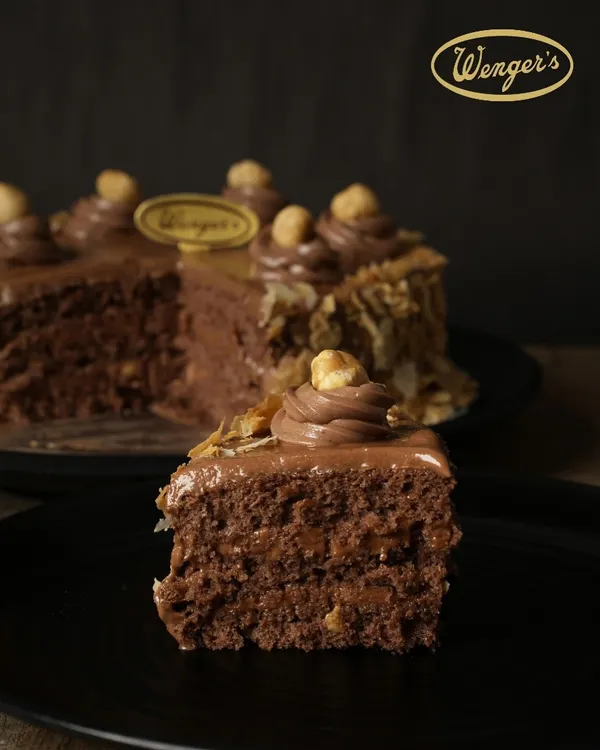 A perfect slice of our Nutella Hazelnut Cake. You can see the layers of moist chocolate sponge and rich Nutella cream, with a satisfying crunch from the nougat. It’s a slice of pure happiness.