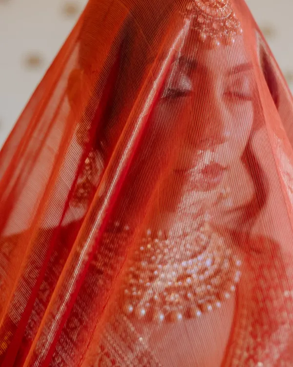 A bride's serene expression seen through her sheer red dupatta, a moment of quiet contemplation.