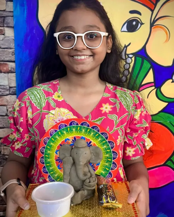 I love seeing the pride on a child's face when they complete their masterpiece. Here, a young artist proudly displays her handmade clay Ganesha idol, sculpted and decorated during our festive workshop. This is a great example of our hands-on clay modeling sessions for kids.