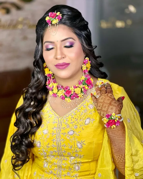 A beautiful bride ready for her Haldi ceremony. She is wearing a vibrant set of pink and yellow floral jewellery that perfectly complements her yellow outfit.