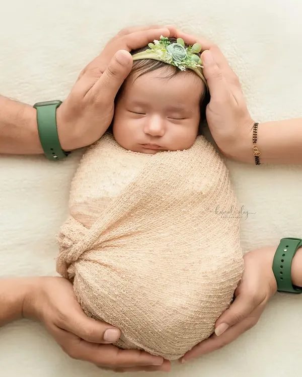 A newborn is held securely by their parents' hands, showcasing a classic and safe pose that emphasizes the baby's small size and the family's protection.